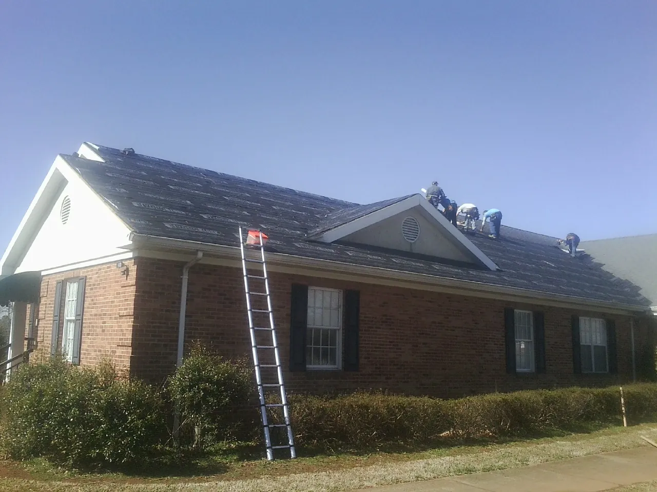 Crew tearing shingles off a brick ranch roof with a ladder set — Emergency Roof Repair work by our crew in Chickamauga