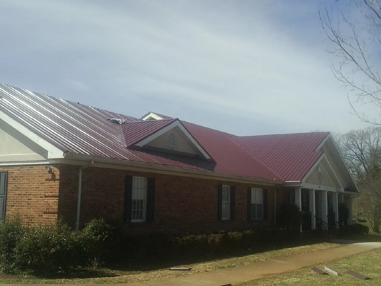 Red metal roof with gabled entries on a long brick building, from a Hail Damage Roof Repair job in Chickamauga