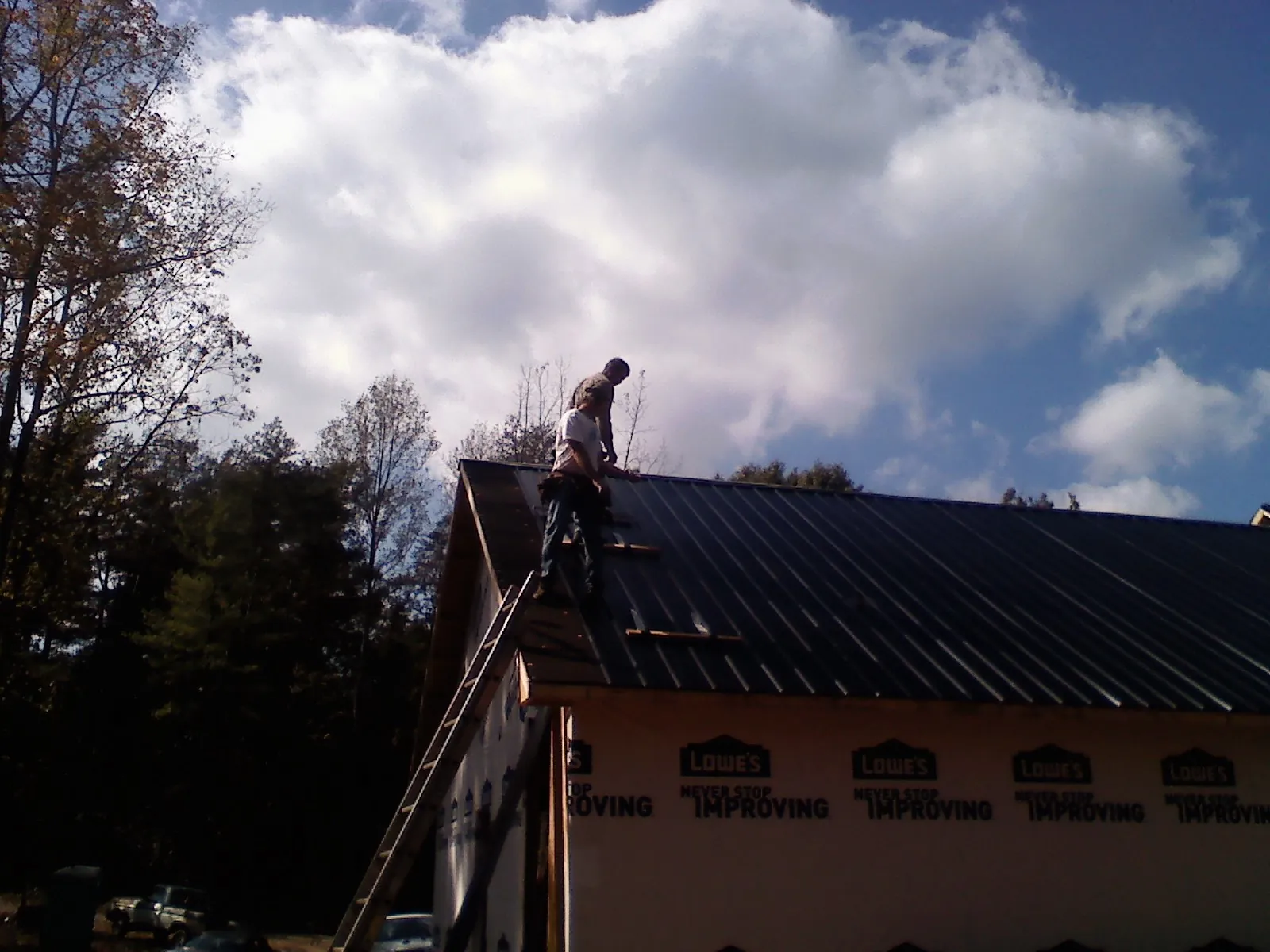 Roofer fastening dark metal panels high against a cloudy sky, from a Roof Inspection job in Chickamauga