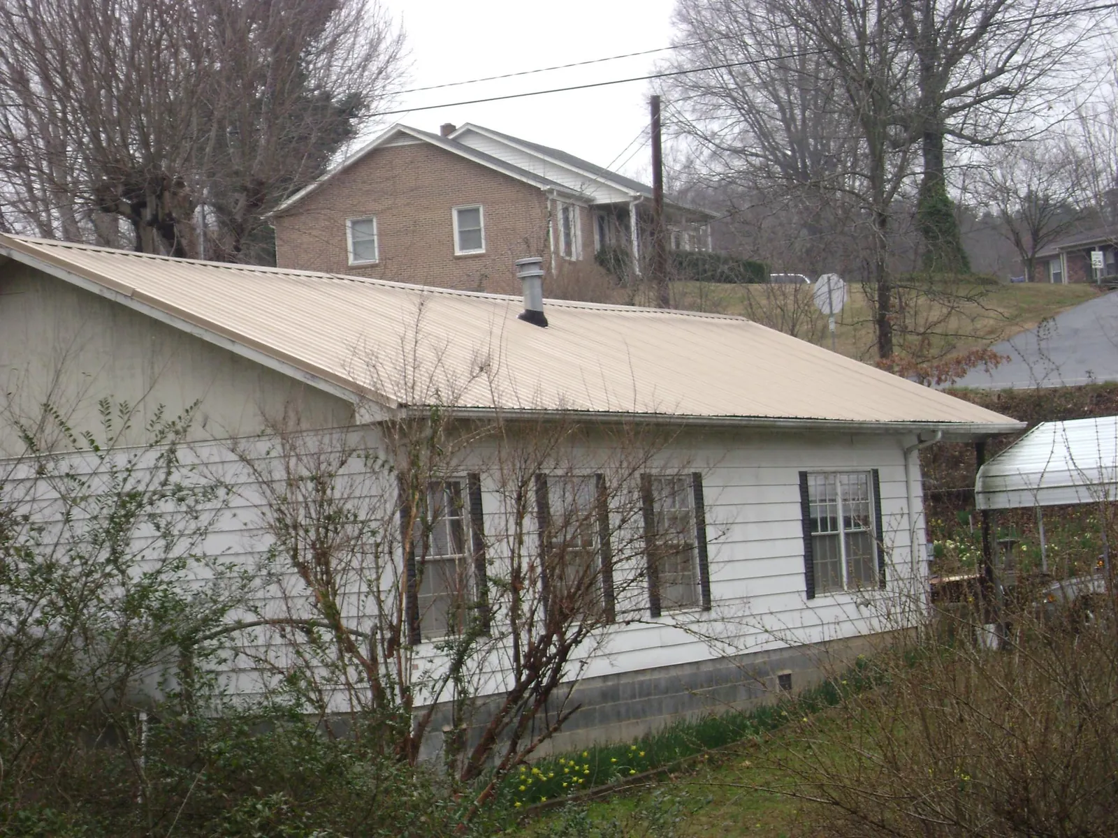Tan metal roof on a white sided house set into a hillside — Commercial Roofing by Roofing Brothers in Chickamauga